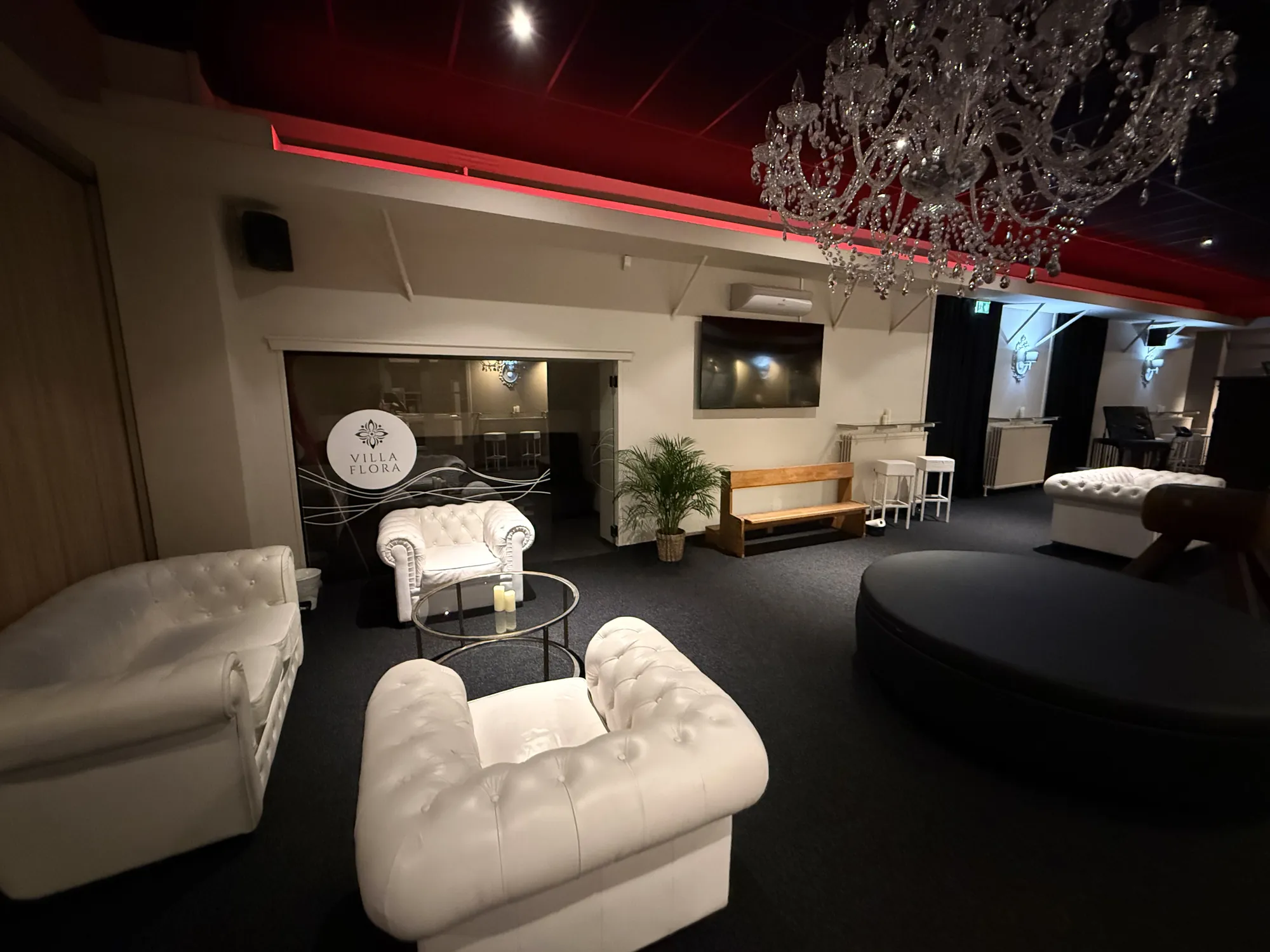 Lounge with white chesterfield sofas, a crystal chandelier and red ceiling light